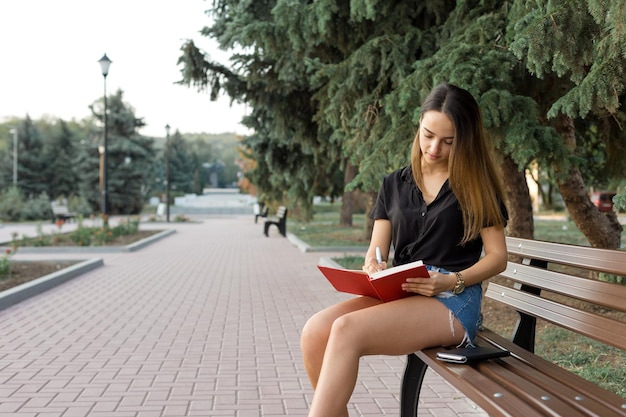 Una niña se sienta en un banco en un parque y toma notas Vestida con un estilo libre Mujer de negocios hablando por teléfono con los clientes