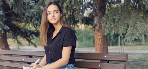 Una niña se sienta en un banco en un parque y toma notas Vestida con un estilo libre Mujer de negocios hablando por teléfono con los clientes