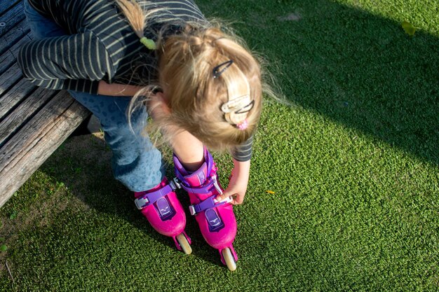 Una niña se sienta en un banco y se pone patines rosas