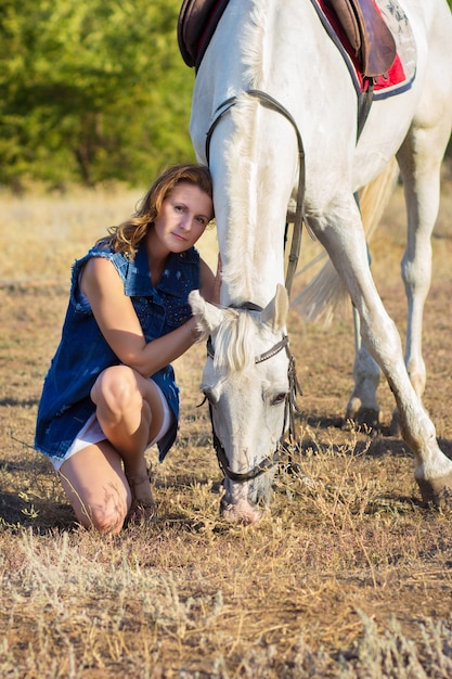 La niña se sienta cerca de un caballo blanco.