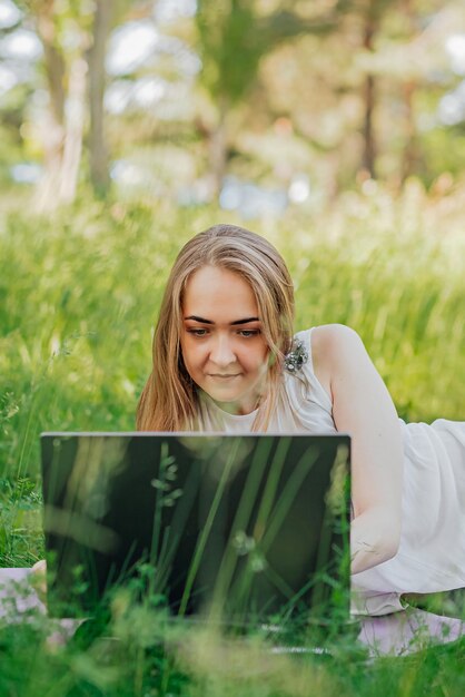 La niña se sienta en el césped y usa una computadora portátil Concepto de tecnología de estilo de vida educativo concepto de aprendizaje al aire libre