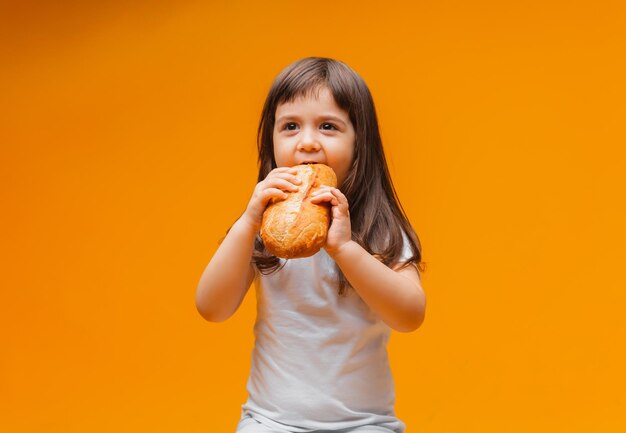 Una niña se sienta en un cubo sobre un fondo amarillo y come una hogaza de pan de productos naturales de alimentos saludables