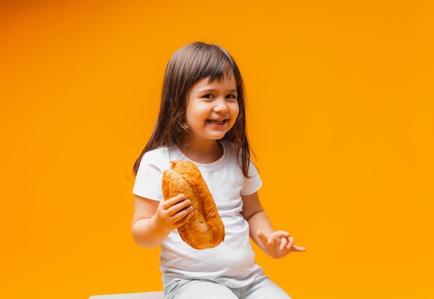 Una niña se sienta en un cubo sobre un fondo amarillo y come una hogaza de pan de productos naturales de alimentos saludables