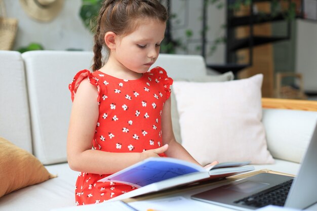 La niña se sienta en el deslizamiento en casa y hace la tarea, el autoestudio del material, el libro de lectura. El concepto de educación a distancia.