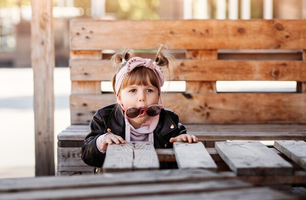 Una niña se sienta y se divierte en un banco en el parque. Tiempo de infancia.