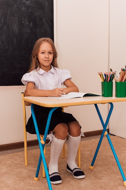 La niña se sienta en la lección en el escritorio.