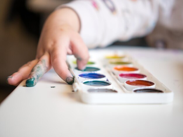 La niña se sienta a la mesa y dibuja con los dedos en el cuaderno de bocetos La creatividad de los niños Pasatiempos de los niños