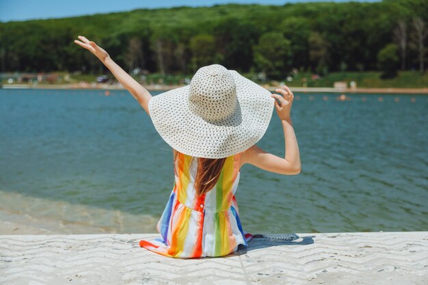 Una niña se sienta en un muelle cerca del lago de la ciudad al aire libre vacaciones de verano