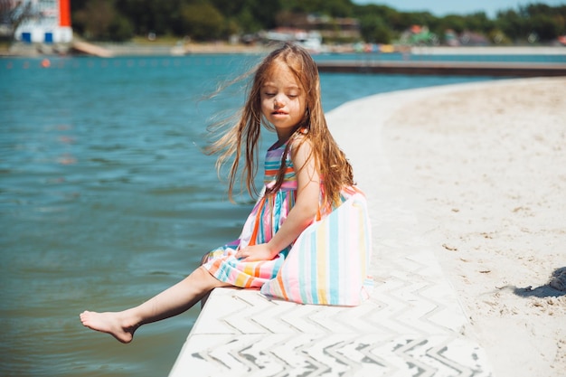 Una niña se sienta en un muelle cerca del lago de la ciudad al aire libre vacaciones de verano