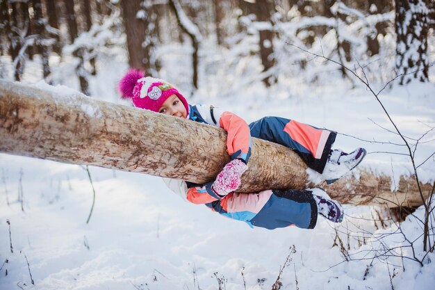 La niña se sienta en la nieve con un mono en el bosque