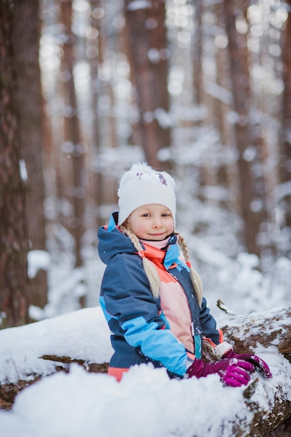 La niña se sienta en la nieve con un mono en el bosque