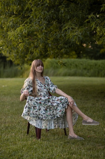 una niña se sienta en un parque en un sillón con un vestido de flores vintage. Vestido retro y ambiente vintage.