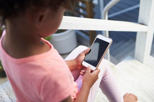 La niña se sienta en los pasos al aire libre jugando con el teléfono móvil