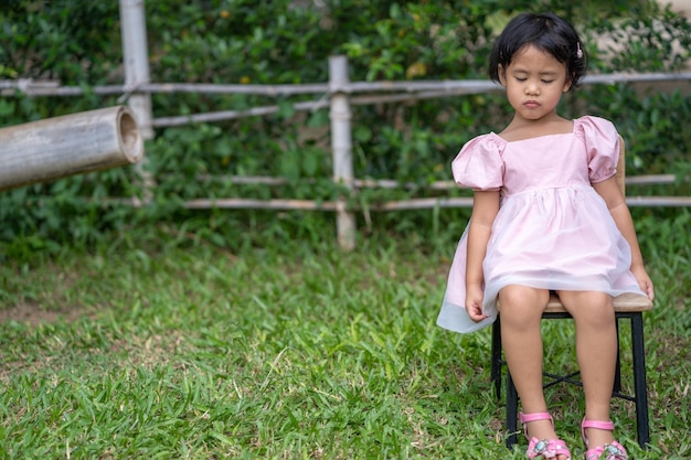 Una niña se sienta en una silla en un jardín.