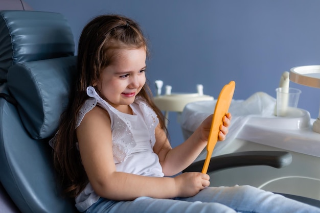 Una niña se sienta en una silla y mira su espejo.