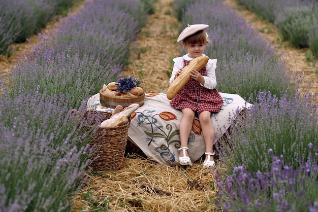 La niña se sienta sobre un mantel bordado y come pan.