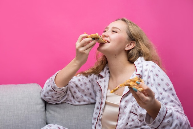 La niña se sienta en el sofá y come pizza.