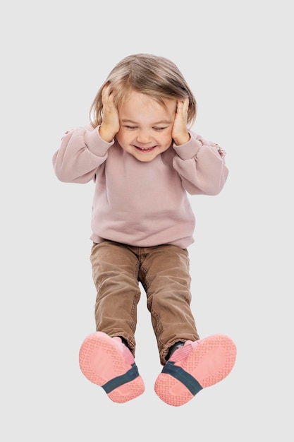 Una niña se sienta y sostiene su cabeza. Riendo lindo bebé con un suéter rosa. Aislado en un fondo gris claro. Vertical.