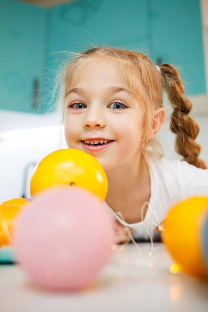 Una niña de siete años lleva una camiseta blanca. Juega con mandarinas maduras
