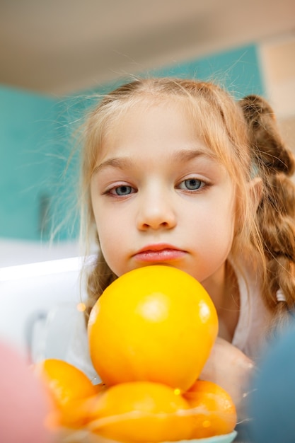 Una niña de siete años lleva una camiseta blanca. Juega con mandarinas maduras