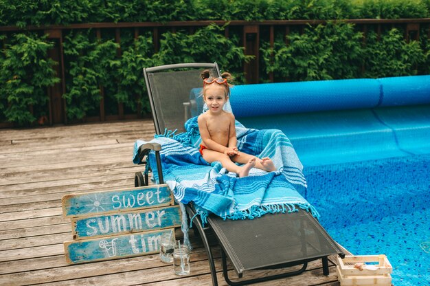 niña en una silla junto a la piscina