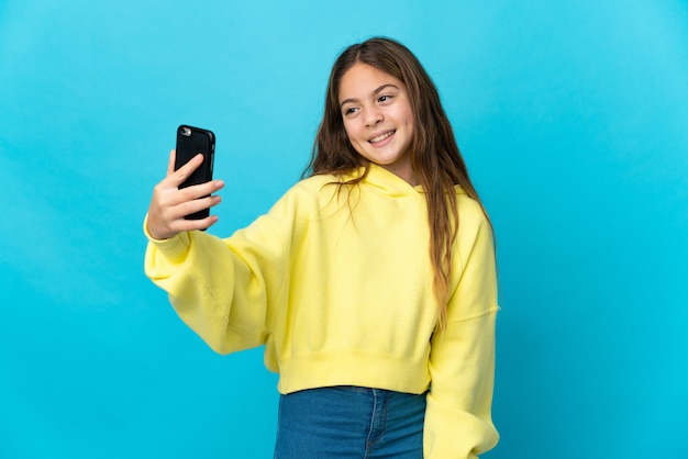 Niña sobre fondo azul aislado haciendo un selfie