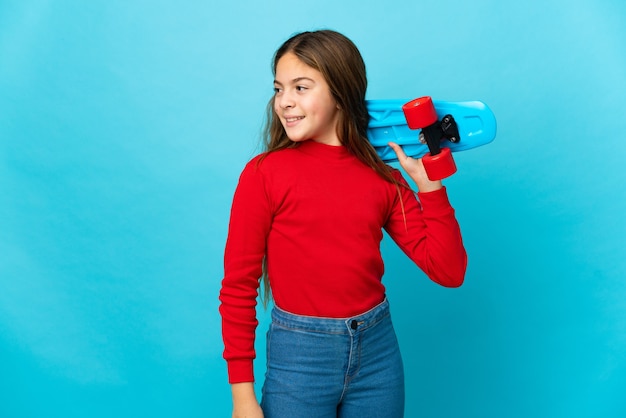 Niña sobre fondo azul aislado con un patín con expresión feliz