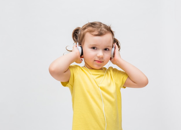 Una niña sobre un fondo blanco en una camiseta amarilla. La niña escucha música a través de auriculares.