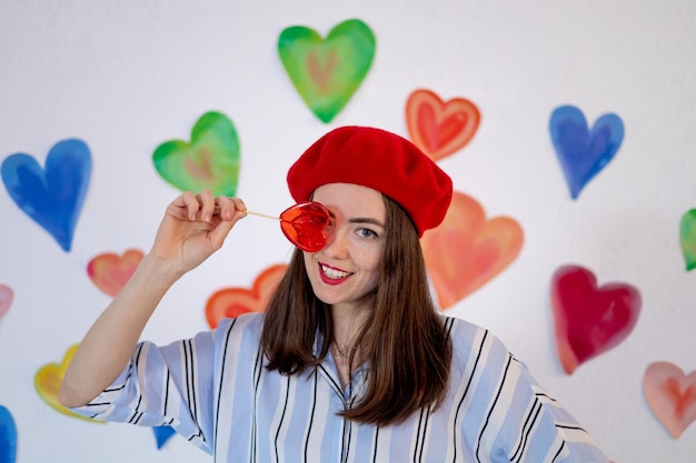 Una niña sobre un fondo de corazones coloridos y brillantes con un corazón de piruleta roja sonríe cerrando los ojos el concepto del amor del día de san valentín