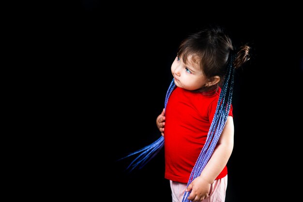 Una niña sobre un fondo negro con coletas afro, trenzadas artificiales en bandas elásticas y se puso lindo