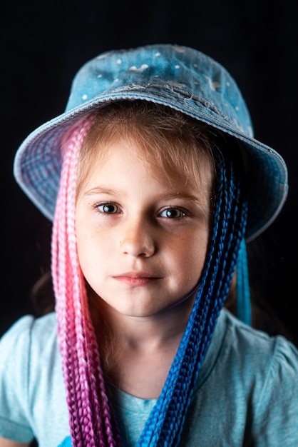 Niña sobre un fondo negro con coletas de bandas elásticas afro azules y rosas en una banda elástica ...