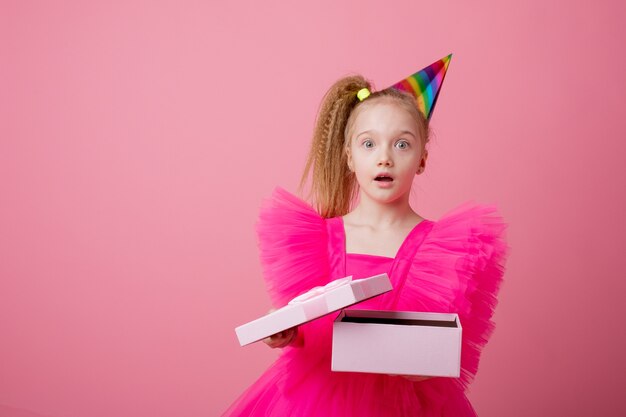 Una niña sobre un fondo rosa abre un regalo celebrando su cumpleaños