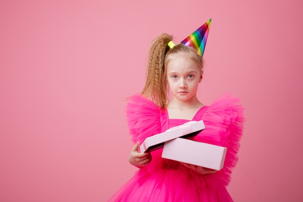 Una niña sobre un fondo rosa abre un regalo celebrando su cumpleaños