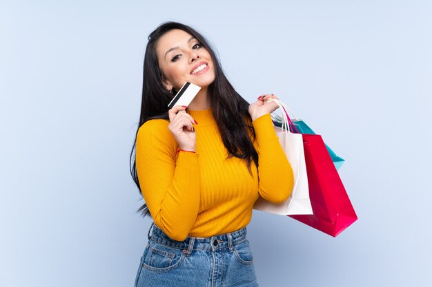 Niña sobre pared azul con bolsas de compra y una tarjeta de crédito