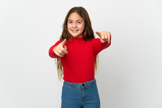 Niña sobre pared blanca aislada apuntando hacia el frente con expresión feliz