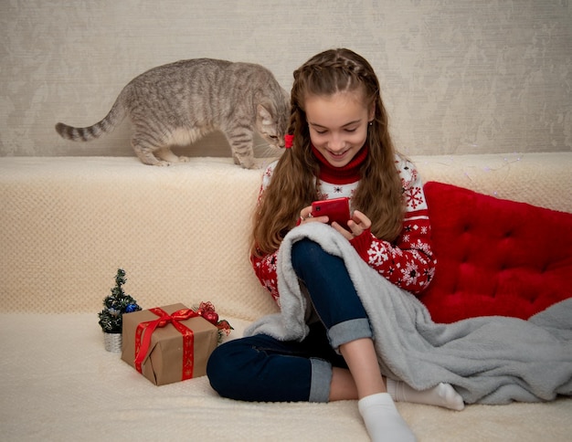 Una niña en el sofá y mira el teléfono celular Junto a la computadora portátil al gato británico Navidad Año Nuevo