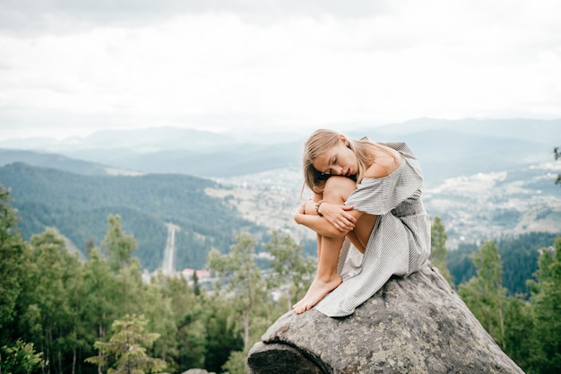 Niña solitaria se sienta en piedra en la cima de la montaña