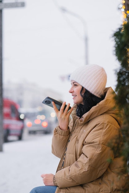 Una niña con sombrero y abrigo graba un mensaje de voz afuera en invierno y se ríe