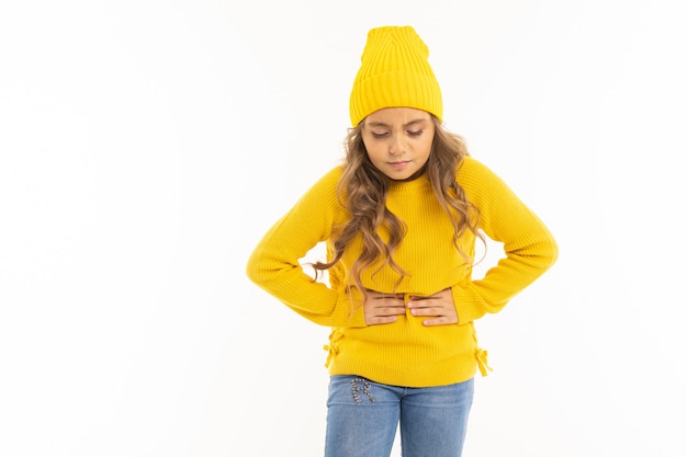 Foto niña de sombrero amarillo se aferra a un estómago en blanco