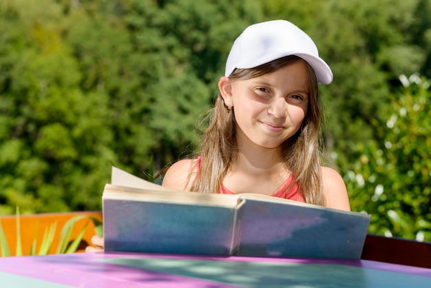 Una niña con sombrero blanco, lee un libro, afuera