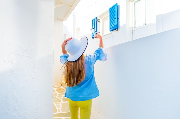 Niña con sombrero blanco toma una foto de la vista griega en una calle en un día