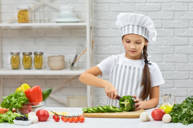 Niña con sombrero de chef y un delantal cortando pimiento verde