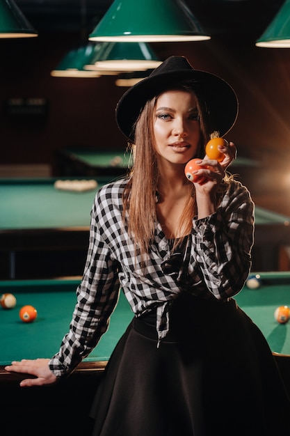 Una niña con un sombrero en un club de billar con bolas en sus manos. Jugar al billar.