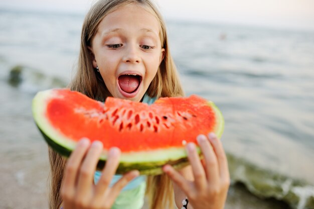 La niña en el sombrero come con entusiasmo la sandía jugosa en el fondo del mar