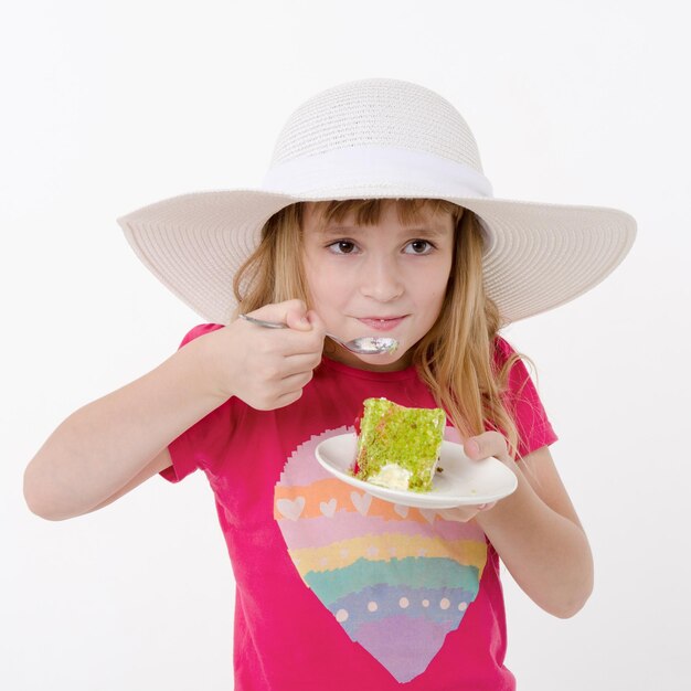 Niña con sombrero comiendo delicioso pastel de crema dulce Retrato de estudio sobre fondo blanco