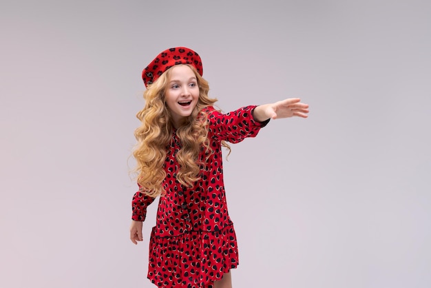 Niña con sombrero de estilo francés señala con el dedo al lado de la niña feliz con el pelo largo y rizado en un b ...