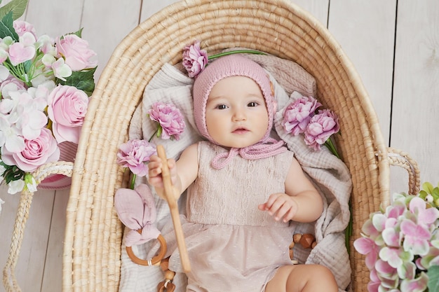 Niña con sombrero de flores en cesta de mimbre con sonajero de madera Postal Día de la Madre y Pascua Día de la Protección de los Niños Día Mundial de la Felicidad Niño sonriente