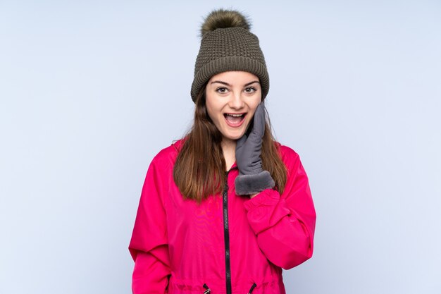 Niña con sombrero de invierno aislado en azul con sorpresa y expresión facial conmocionada