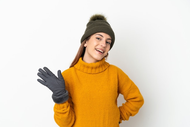 Niña con sombrero de invierno aislado sobre fondo blanco saludando con la mano con expresión feliz