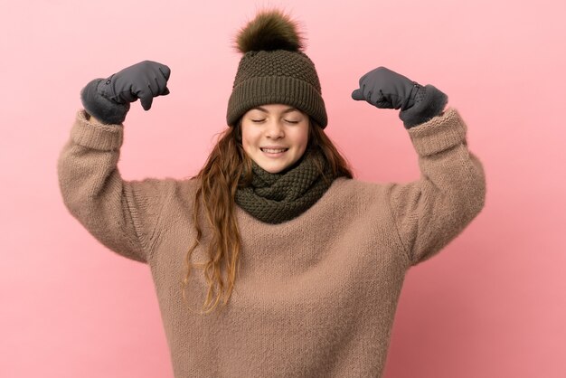 Niña con sombrero de invierno aislado sobre fondo rosa haciendo gesto fuerte